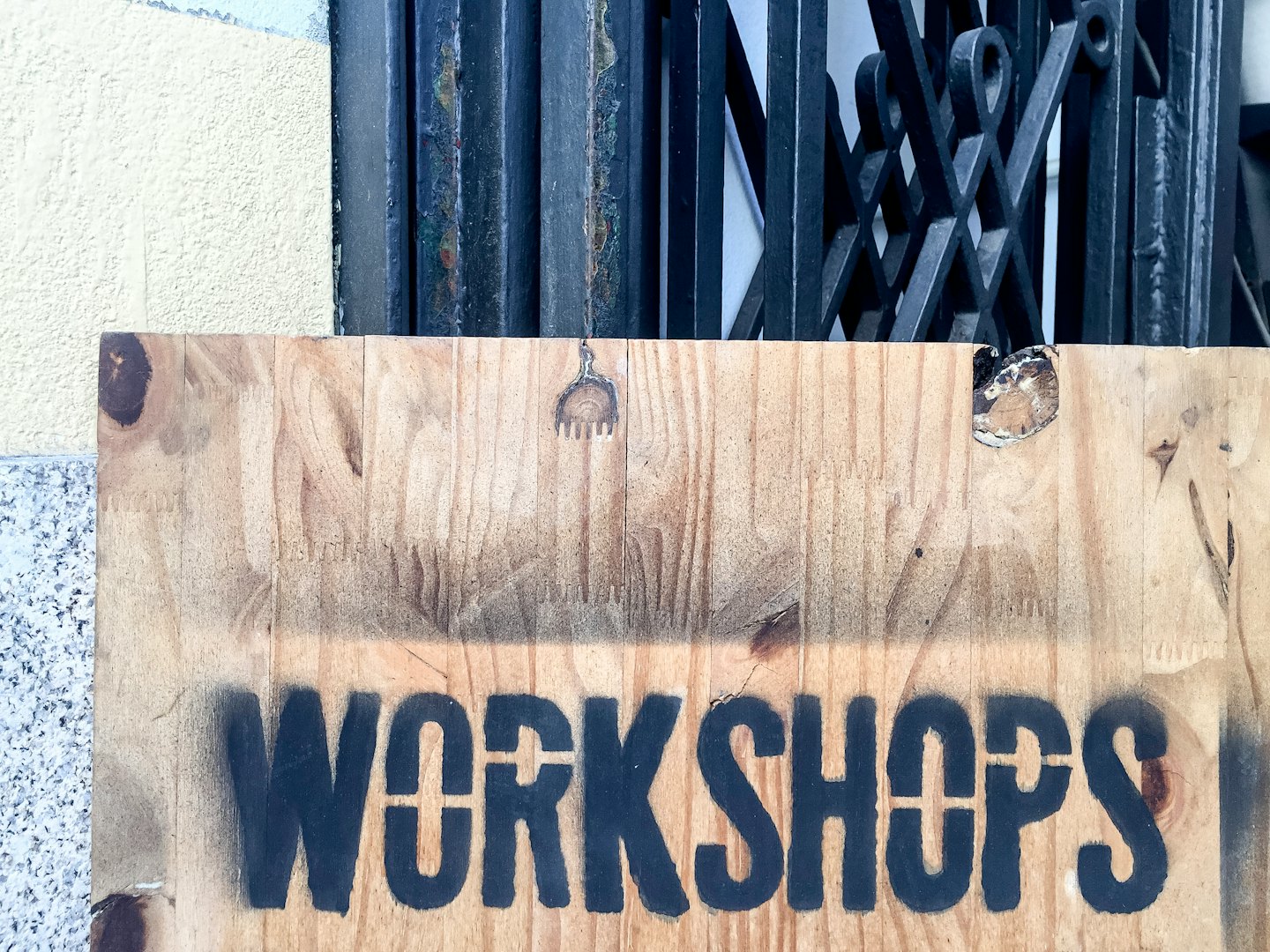 Wooden sign for workshops leaning against a stucco wall.
