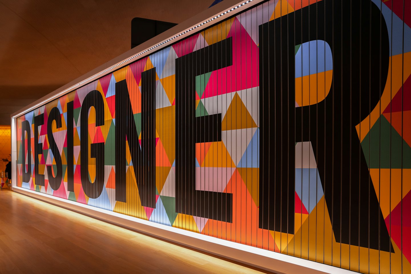 Illuminated word "DESIGNER" on a colorful geometric wall.
