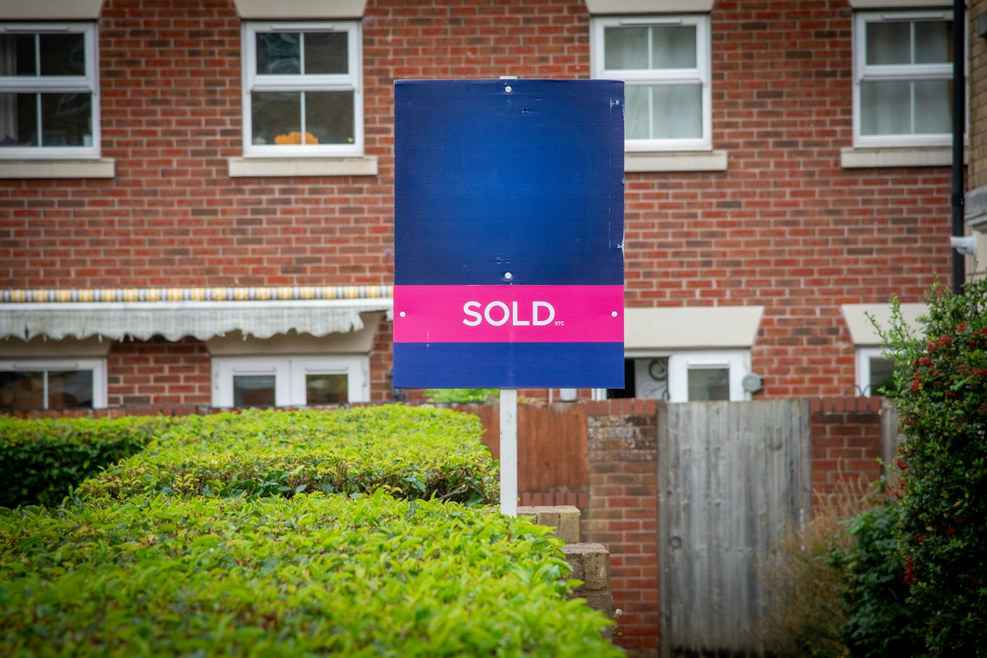 A sold sign stands in front of a red brick house.
